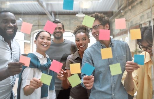 Working on business project together. Group of young and positive coworkers putting colorful sticky notes on a glass window in the creative office